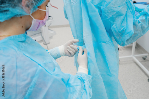 Fotografija The nurse helps the surgeon put on a sterile gown before surgery uniform in the