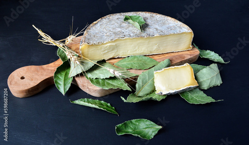 Saint Nectaire cheese with bay leaf on a cutting board. It is an Auvergne cheese and a mountain cheese made with cow’s milk. photo