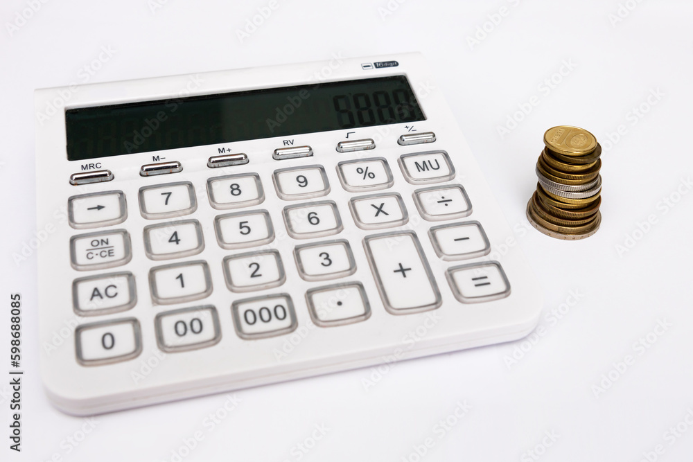 stack of coins next to a calculator on a white background stack of coins next to a calculator on a white background