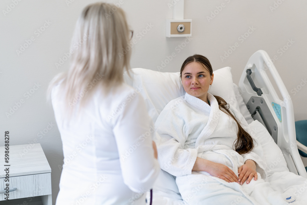 Fototapeta premium a female doctor standing by the bed in a hospital room and discussing a treatment plan with a young female patient