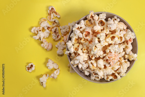 Paper cup with popcorn on yellow background, top view