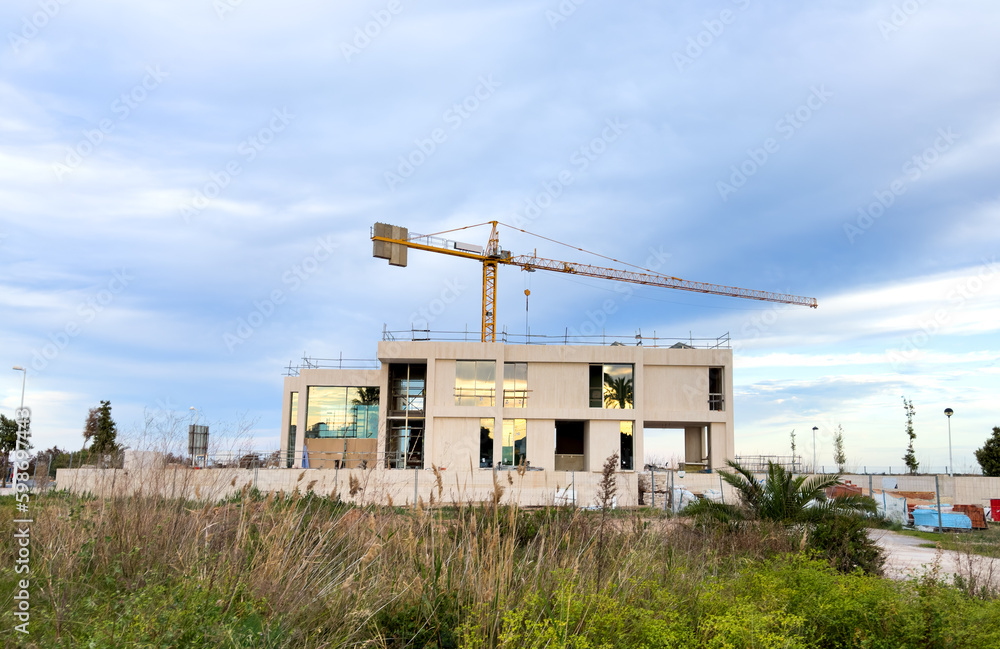 Villa under construction. Tower crane on construction site. Luxury villa construction near beach Mediterranean sea. Construction of modern house on coastline. Townhouse, Home renovation at ocean. Villa under construction. Tower crane on construction site. Luxury villa construction near beach Mediterranean sea. Construction of modern house on coastline. Townhouse, Home renovation at ocean.