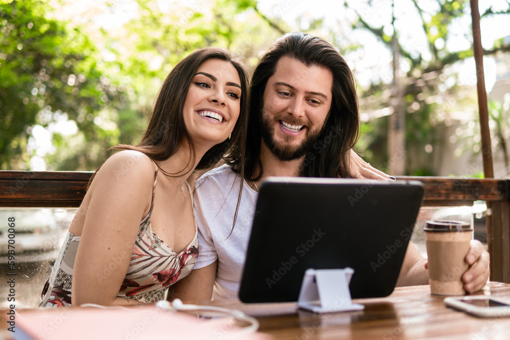 brazilian couple smiling and looking at tablet screen in table outside brazilian couple smiling and looking at tablet screen in table outside