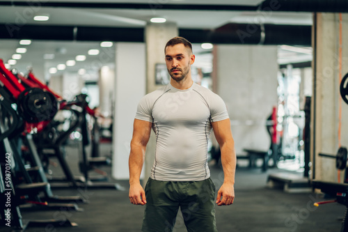 Portrait of a serious strong sportsman posing in a gym with exercise equipment in a blurry background.
