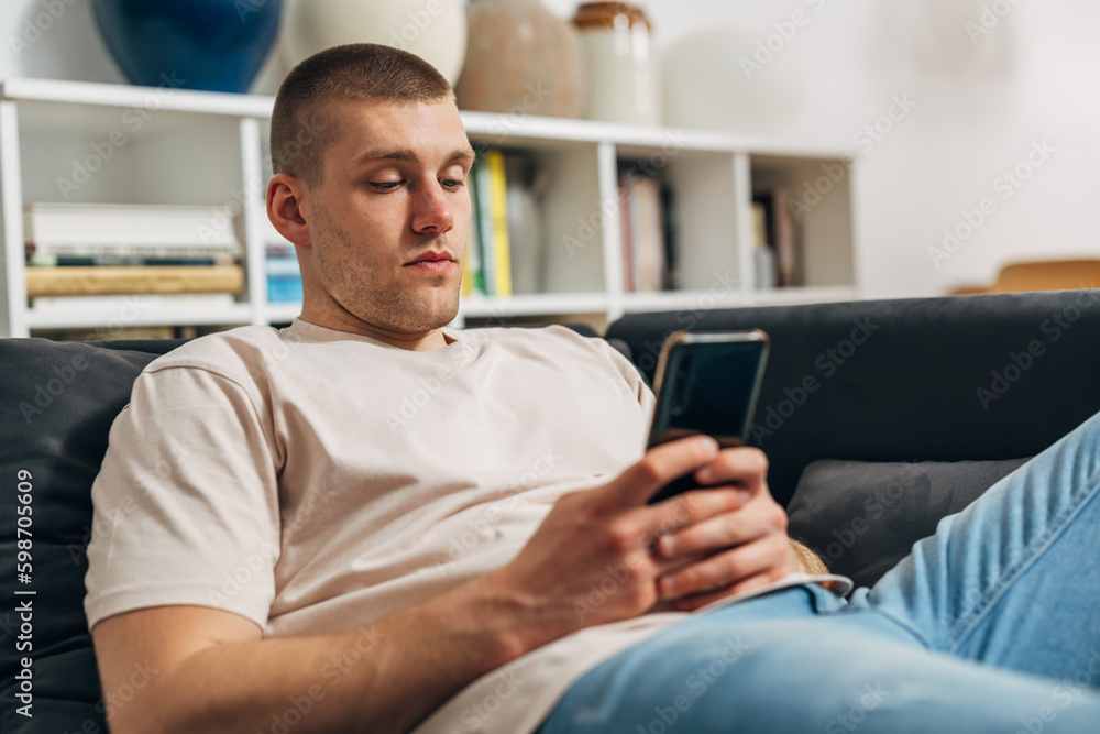 A handsome Caucasian man is sitting on the sofa and using his smartphone. A handsome Caucasian man is sitting on the sofa and using his smartphone.