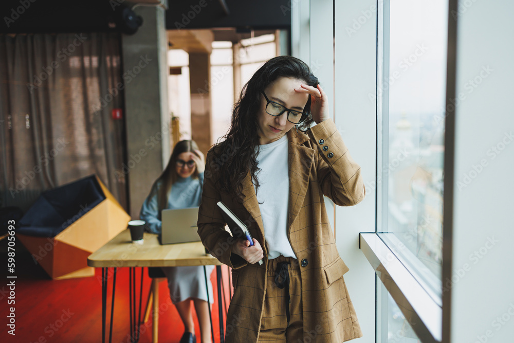 Fototapeta premium A successful woman in glasses works in the office on the background of colleagues. Modern working day in the office. Businesswoman makes notes in a notebook