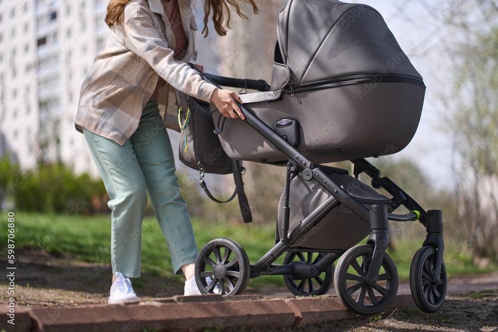 Obraz premium Young Caucasian woman mother, hardly drags a baby stroller with her newborn child up the stairs.