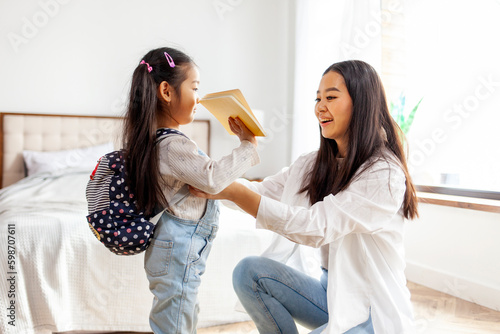 back to school, Korean woman helps her daughter get ready for school and puts her backpack on and supports the girl