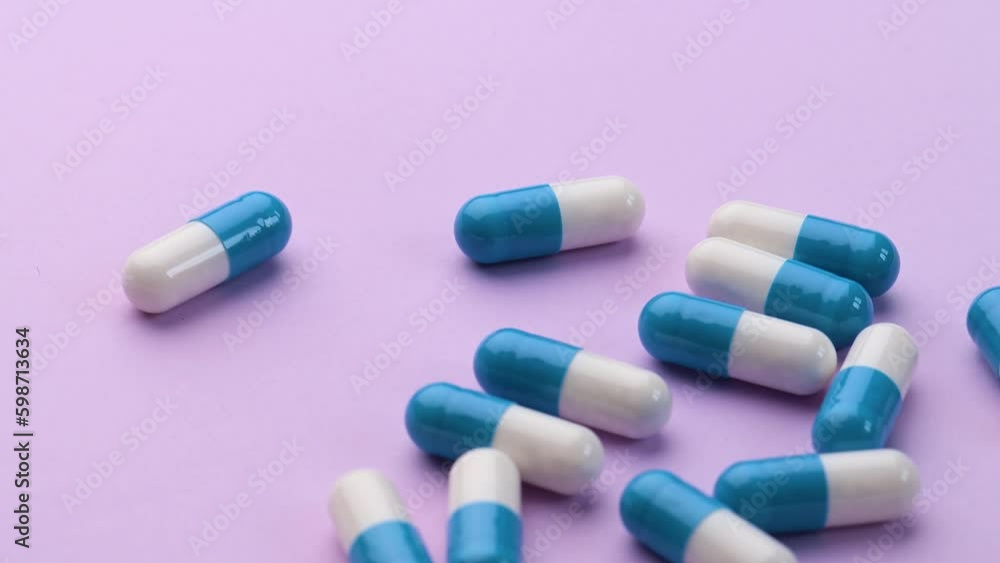 Blue and white medicine pills spread out on a purple table Blue and white medicine pills spread out on a purple table