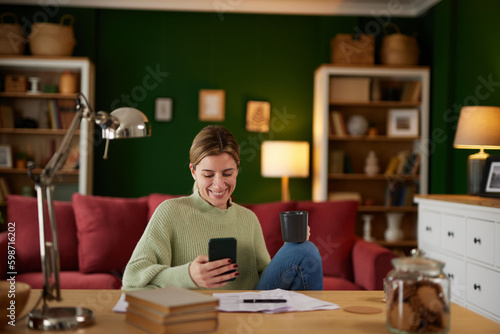 Happy young businesswoman text messaging from home office