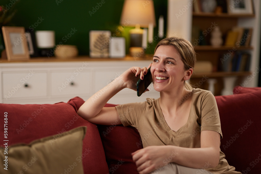 Happy woman talking on mobile phone while relaxing on sofa at home Happy woman talking on mobile phone while relaxing on sofa at home