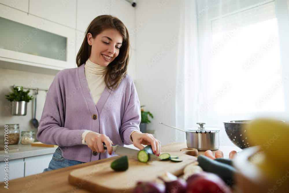 Woman chopping cucumber at the wooden board in the kitchen Woman chopping cucumber at the wooden board in the kitchen