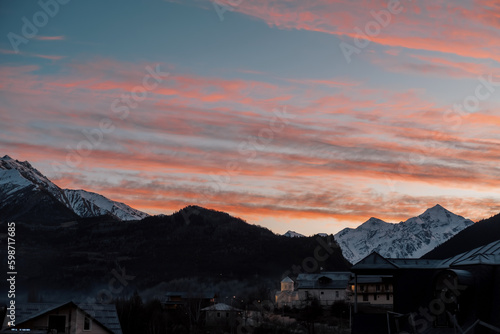 Medieval town with church, sunset and pink clouds above hills against backdrop of snowy peaks of mountains, Mestia Svaneti Georgia