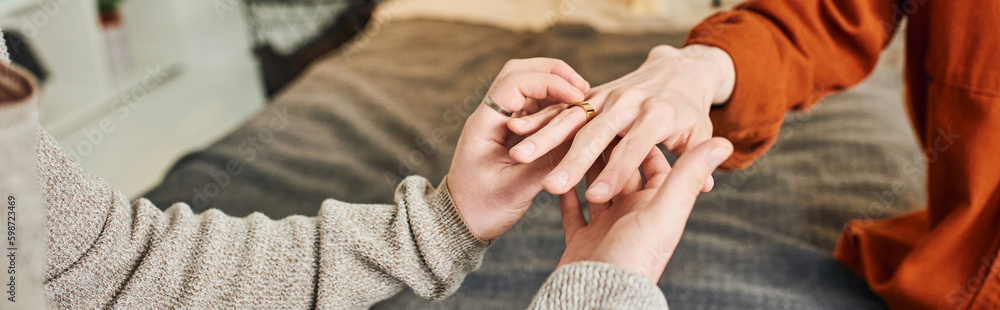 cropped view of gay man wearing wedding ring on hand of boyfriend while making marriage proposal at home, banner. cropped view of gay man wearing wedding ring on hand of boyfriend while making marriage proposal at home, banner.