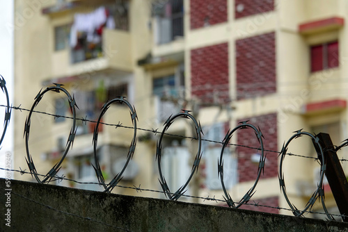 Canvas Print Barbed wire on concrete wall and tall residential building in background