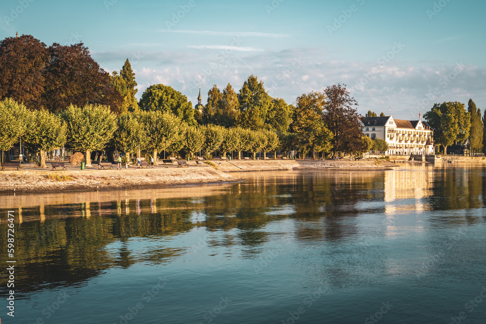 Beautiful sunrise view from Imperia statue at harbor entrance on Steigenberger hotel, shorefront and Lake Constance in early morning hours. Port, Constance, Baden-Württemberg, Germany, Europe. Beautiful sunrise view from Imperia statue at harbor entrance on Steigenberger hotel, shorefront and Lake Constance in early morning hours. Port, Constance, Baden-Württemberg, Germany, Europe.