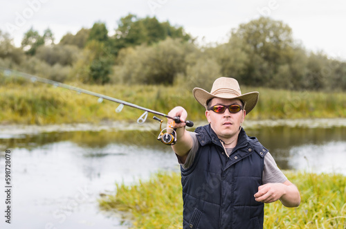 Fisherman in a hat and glasses on the river bank with a spinning rod in his hands.