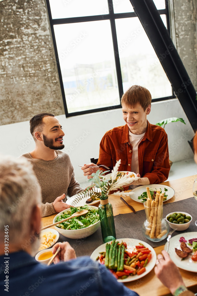 redhead man looking at parents while serving salad near gay partner during family dinner. redhead man looking at parents while serving salad near gay partner during family dinner.
