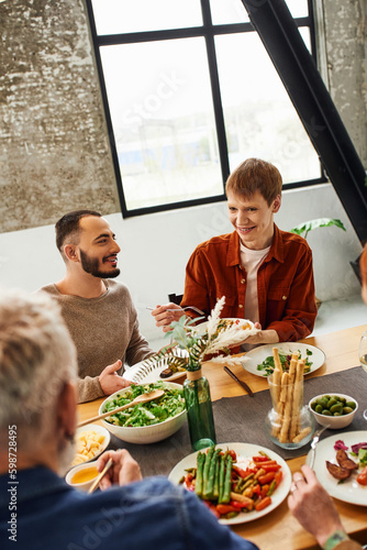 redhead man looking at parents while serving salad near gay partner during family dinner. 