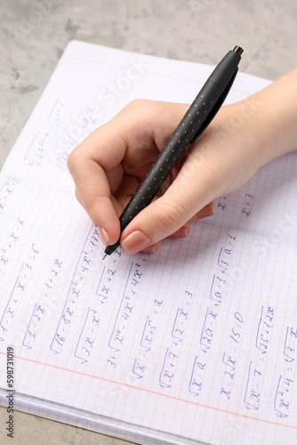 Woman writing maths formulas in copybook with pen, closeup