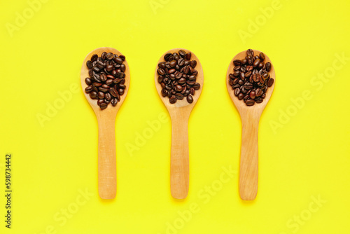 Wooden spoons with coffee beans on yellow background