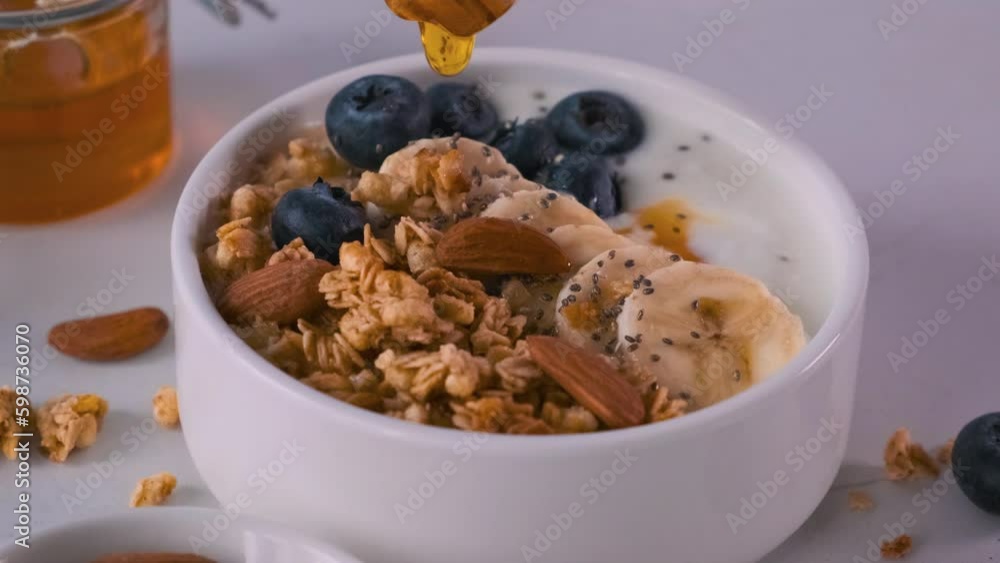Pouring honey into the bowl of greek yogurt with oatmeal granola, banana, blueberry, nuts, chia seeds Generative AI Pouring honey into the bowl of greek yogurt with oatmeal granola, banana, blueberry, nuts, chia seeds Generative AI