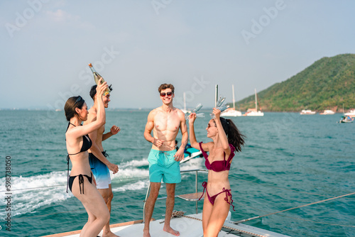 Friends group drink a champagne at outdoor party on yacht. Attractive young men and women hanging out, happy fun to celebrating holiday vacation trip on catamaran sailing boat, Summer relaxation time