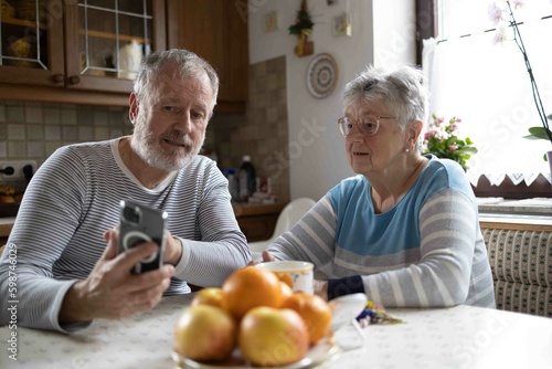 Grey haired senior couple using smartphone in the kitchen at home  