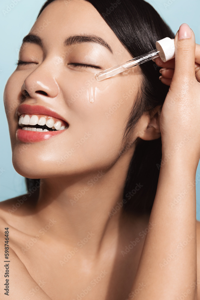Skin care. Beauty portrait of a woman holding a bottle with a dropper near her face. Model using a natural cosmetic product for a hydrated, glowing and healthy facial dermis. Essential oil