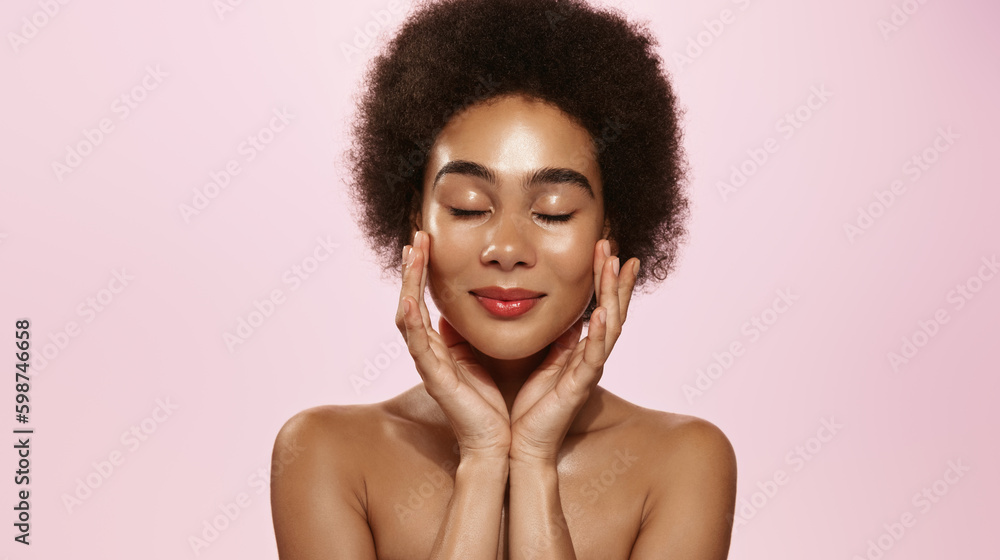 Portrait of smiling young African American woman applying moisturizer on cheeks in bathroom
