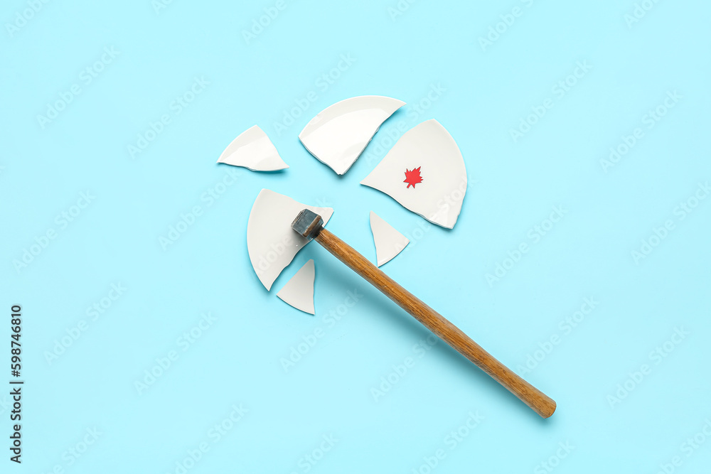 Hammer and broken plate with paper maple leaf on blue background. Canadian flag concept Hammer and broken plate with paper maple leaf on blue background. Canadian flag concept