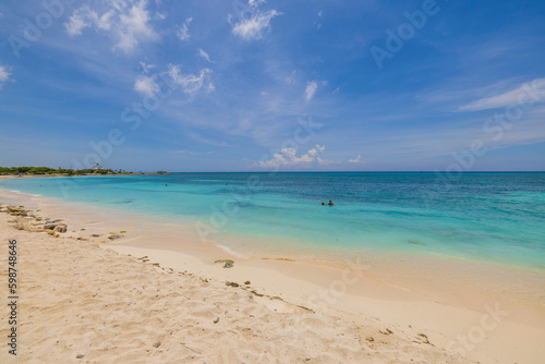Gorgeous coastline landscape view on sunny day. Couple people swimming in water. Aruba. 