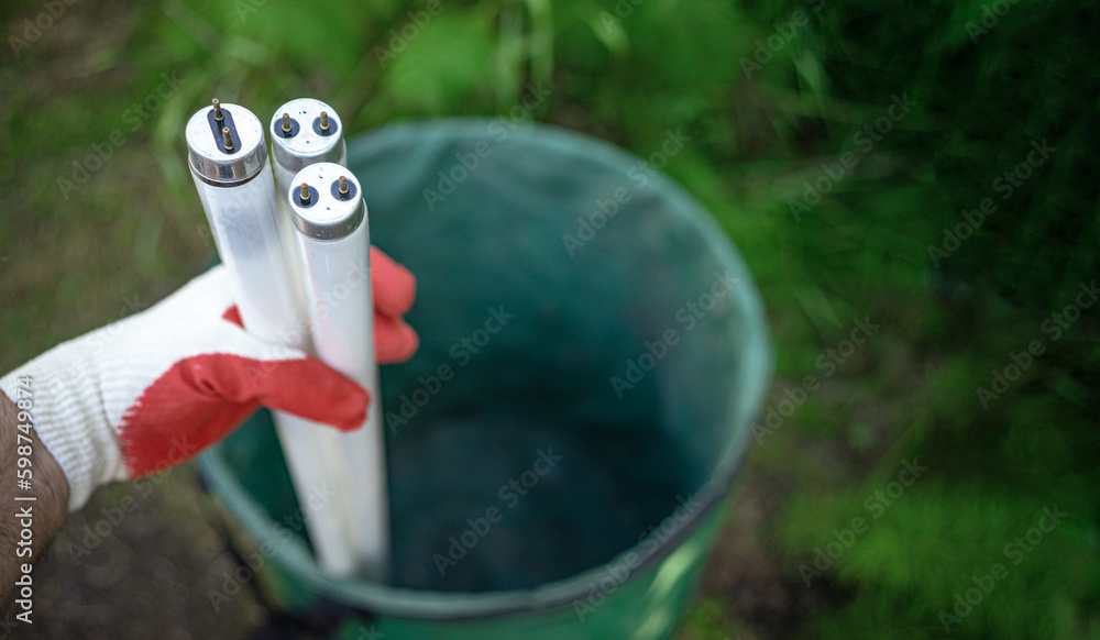 Foto de A gloved hand holds long glass lamps in a trash can.Disposal of