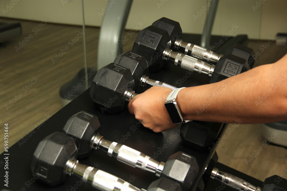 Naklejka premium Dark-haired latino adult man exercises in a gym, muscle strength work for physiotherapy rehabilitation on arm with dumbbells