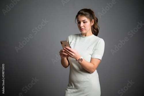 Junge Frau mit braunen Haaren und lockerem Outfit schaut mit konzentriertem Blick auf Handy