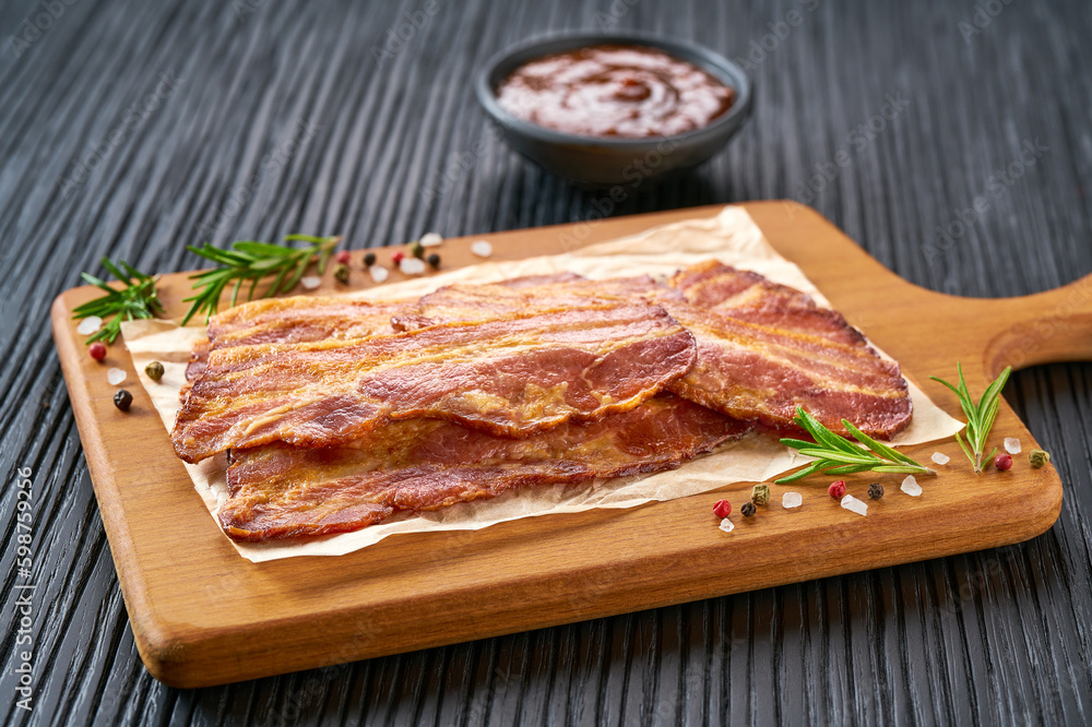 fried bacon strips and bbq sauce on a black table, selective focus. fried bacon strips and bbq sauce on a black table, selective focus.