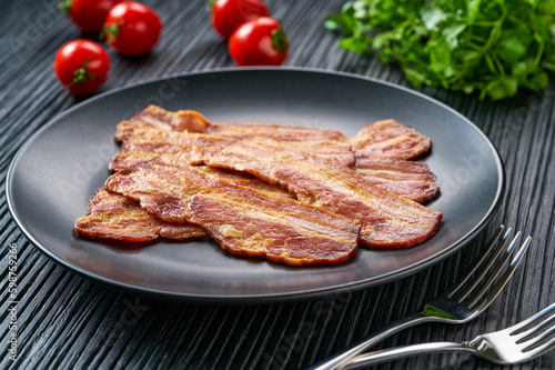 plate with fried bacon and bbq sauce on a black table.  Plate with fried bacon on black  kitchen table.