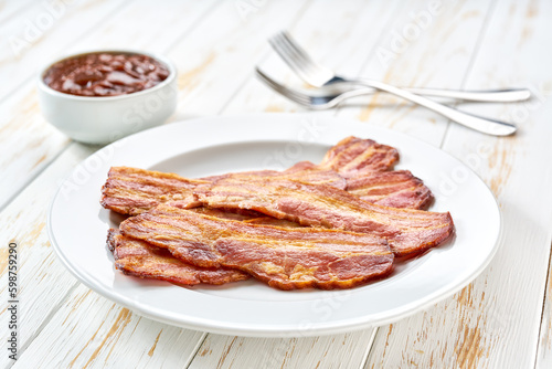plate with fried bacon rashers and bbq sauce on a table, copy space for text. Plate with fried bacon on white kitchen table.