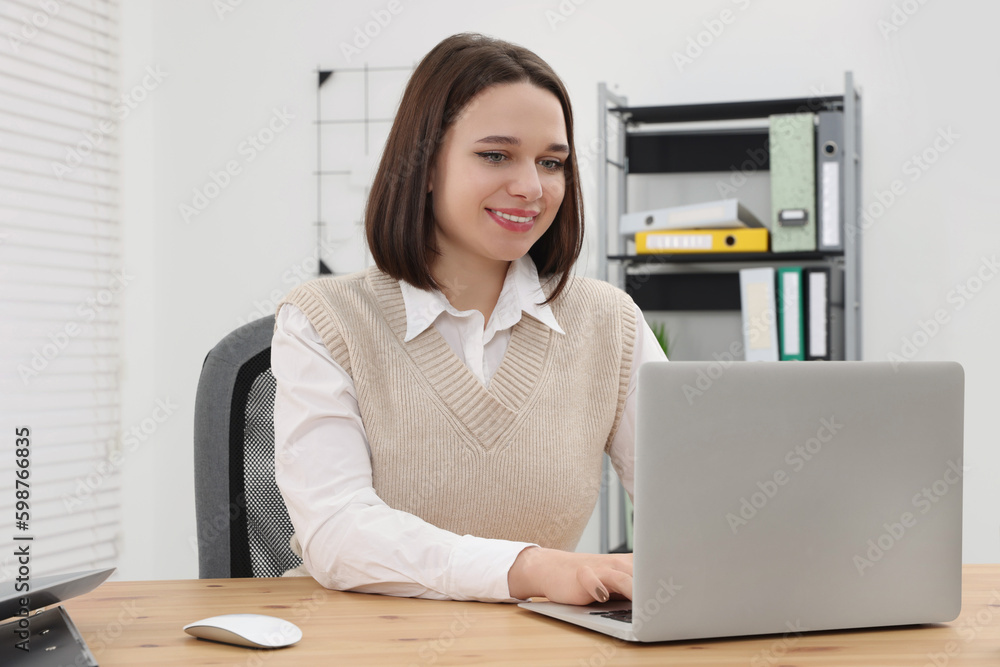 Happy young intern working with laptop at table in modern office Happy young intern working with laptop at table in modern office