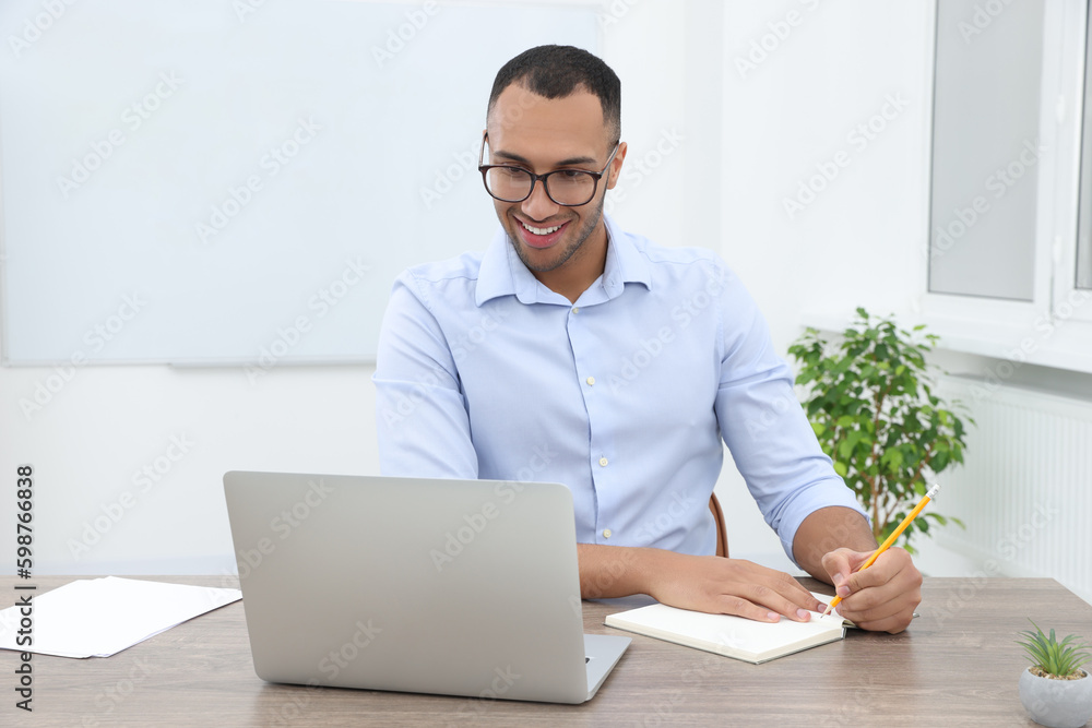 Happy young intern working with laptop at table in modern office Happy young intern working with laptop at table in modern office
