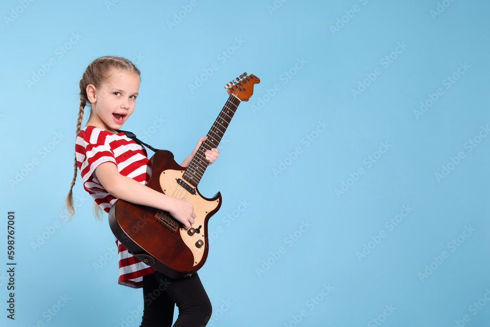 Fototapeta premium Cute girl with electric guitar on light blue background. Space for text