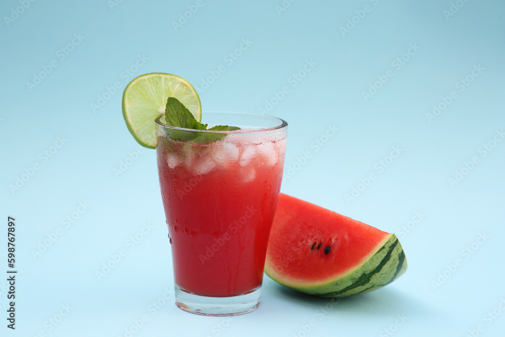 Glass of delicious drink with lime, ice cubes and cut fresh watermelon on light blue background Glass of delicious drink with lime, ice cubes and cut fresh watermelon on light blue background