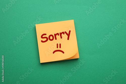 Apology. Sticky note with word Sorry and drawn sad face on green background, top view