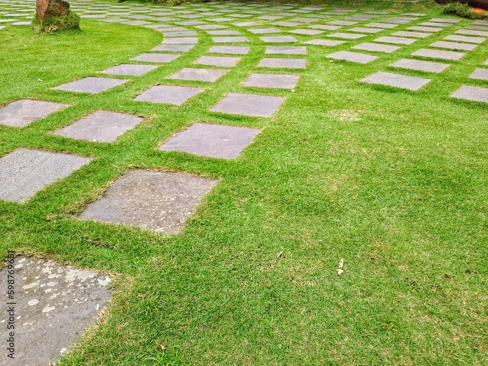 Pattern of square cement floor tiles with green . walkway with green grass in the park. Stone pathway and green grass at park. Garden Stepping Stone Path through Green Grass Law. Pattern of square cement floor tiles with green . walkway with green grass in the park. Stone pathway and green grass at park. Garden Stepping Stone Path through Green Grass Law.