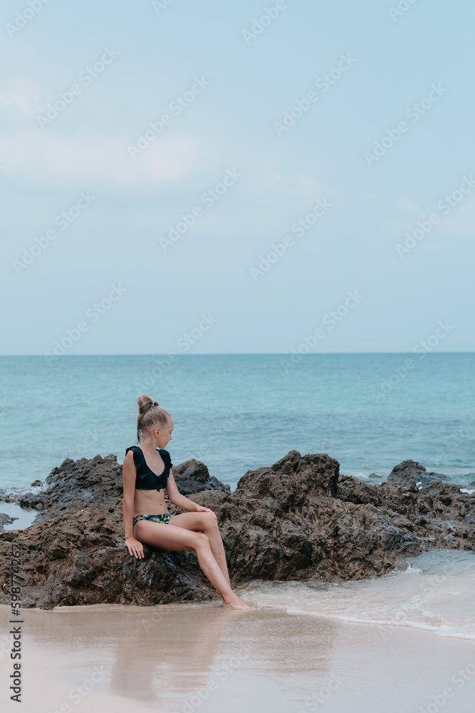 girl sits by the sea on the rocks and enjoys the view, beautiful sea view, children on vacation