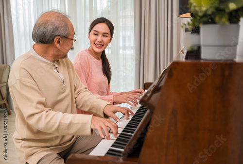 Portrait of happy beautiful Asian woman and her father sitting playing piano and singing together having fun and enjoying in living room at home.