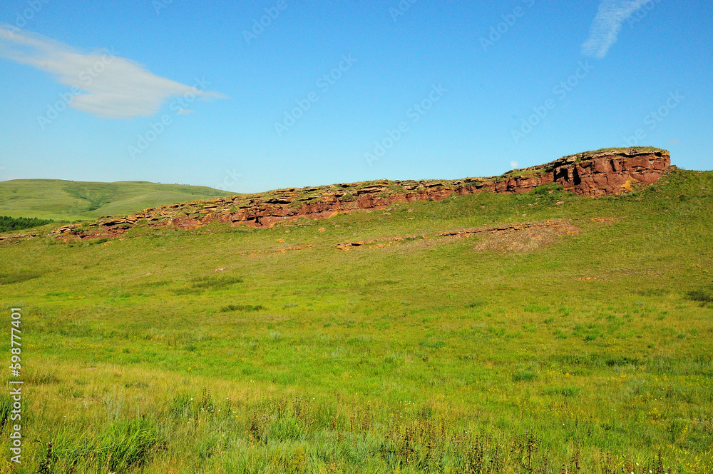 Obraz premium Remains of a ruined ancient red sandstone wall running up the slope to the top of a high gentle hill on a clear summer day.