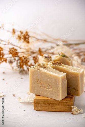 Delicate natural beige handmade soap in a wooden soap dish on a white background with flowers and petals.