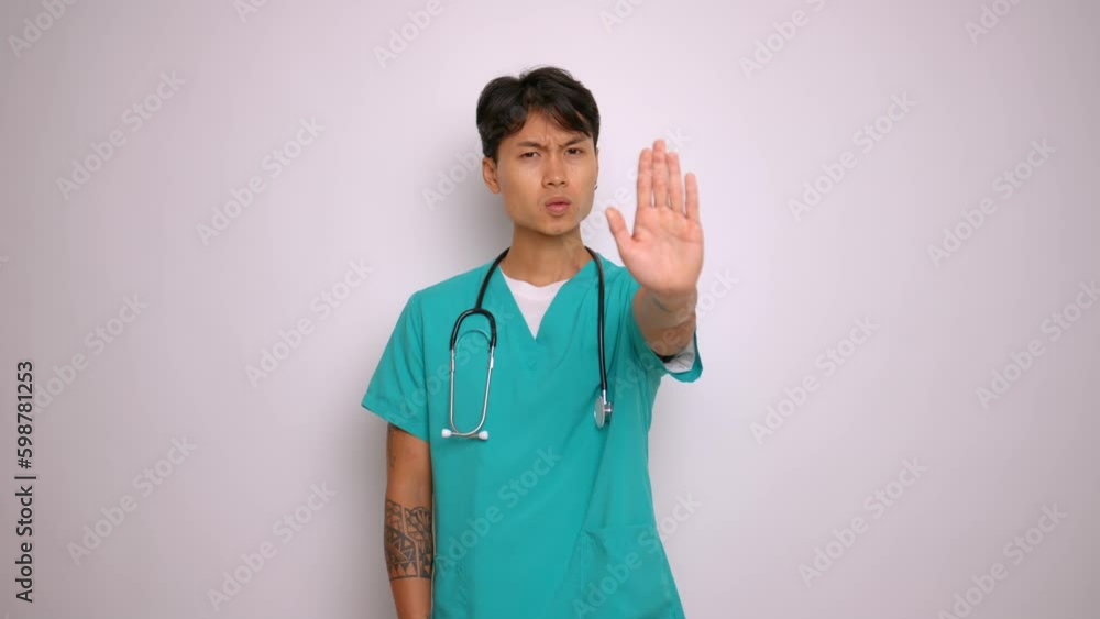 Young medical worker stands on background in studio, dressed in blue medical shirt, has stethoscope around neck, stretches hand forward and shows stop sign with his palm, copy space Generative AI Young medical worker stands on background in studio, dressed in blue medical shirt, has stethoscope around neck, stretches hand forward and shows stop sign with his palm, copy space Generative AI