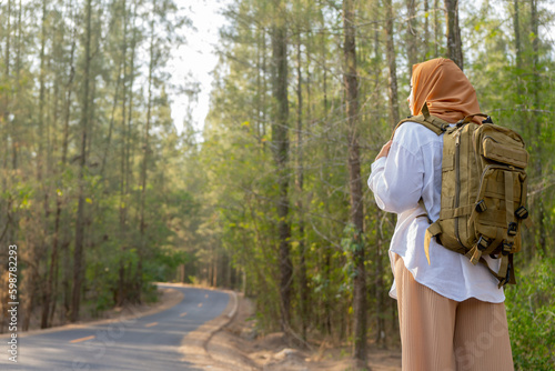 Muslim Asian woman wearing hijab with a backpack and hat hiking in the mountains during the summer season, a traveler walking in the forest. Travel, adventure, and journey concept. © maya1313
